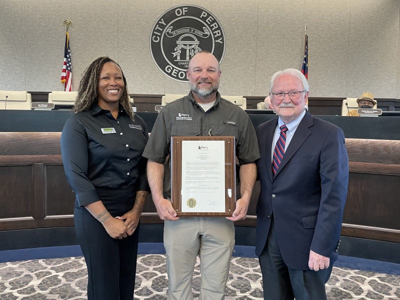 One woman and two men pose for a picture. Man in the middle is holding the proclamation.