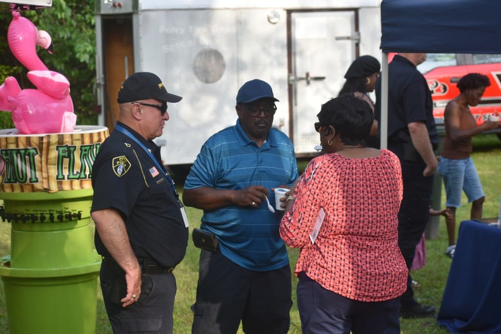 a man in a police uniform speaking to a male and a female in a park