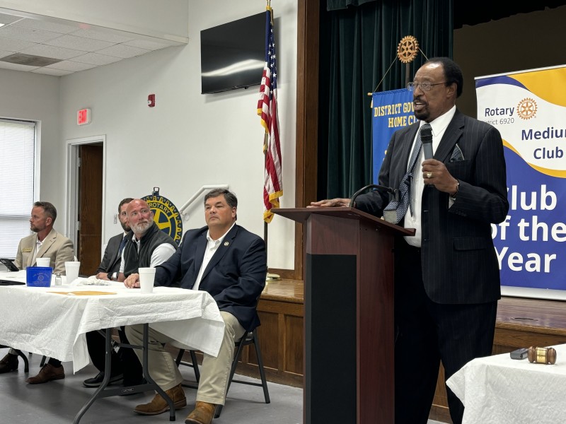 African American male speaking at a podium as other sheriff candidates look and listen.
