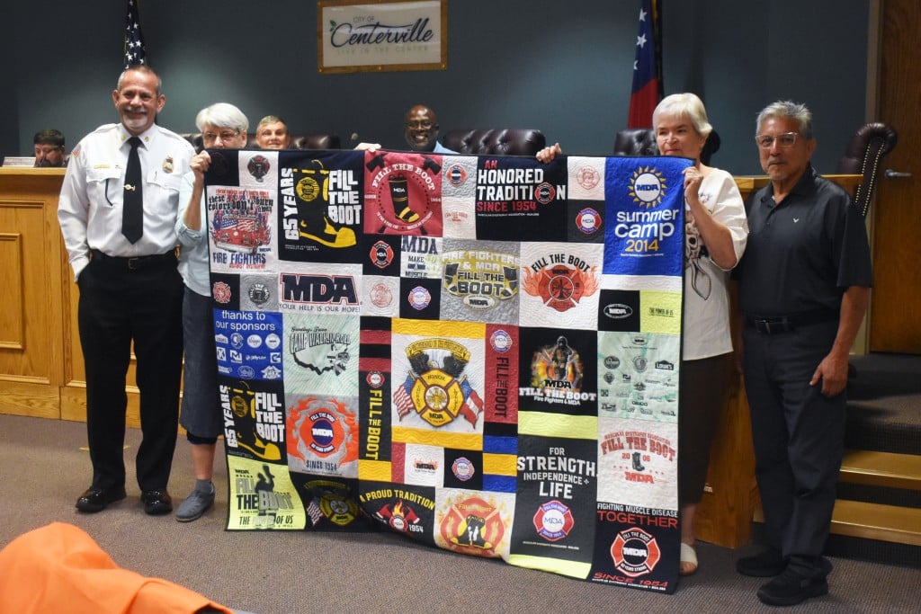 Group of people holding a big quilt.
