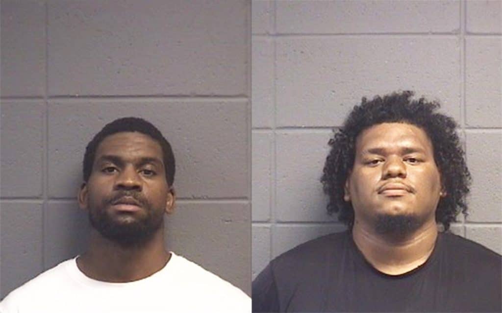 two mugshots along gray brick wall