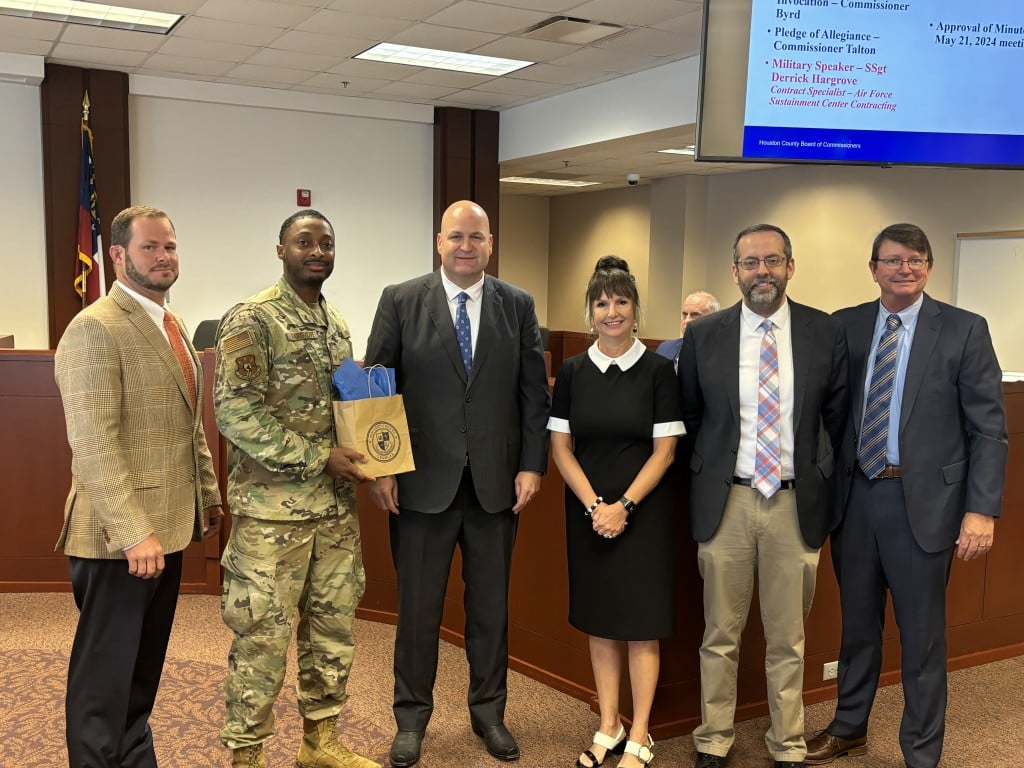five men, one in military uniform and four wearing suits and ties along with one women pose for a picture