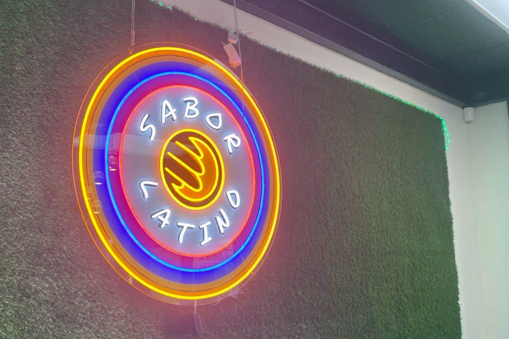 a neon sign on a plant wall that says "sabor latino"