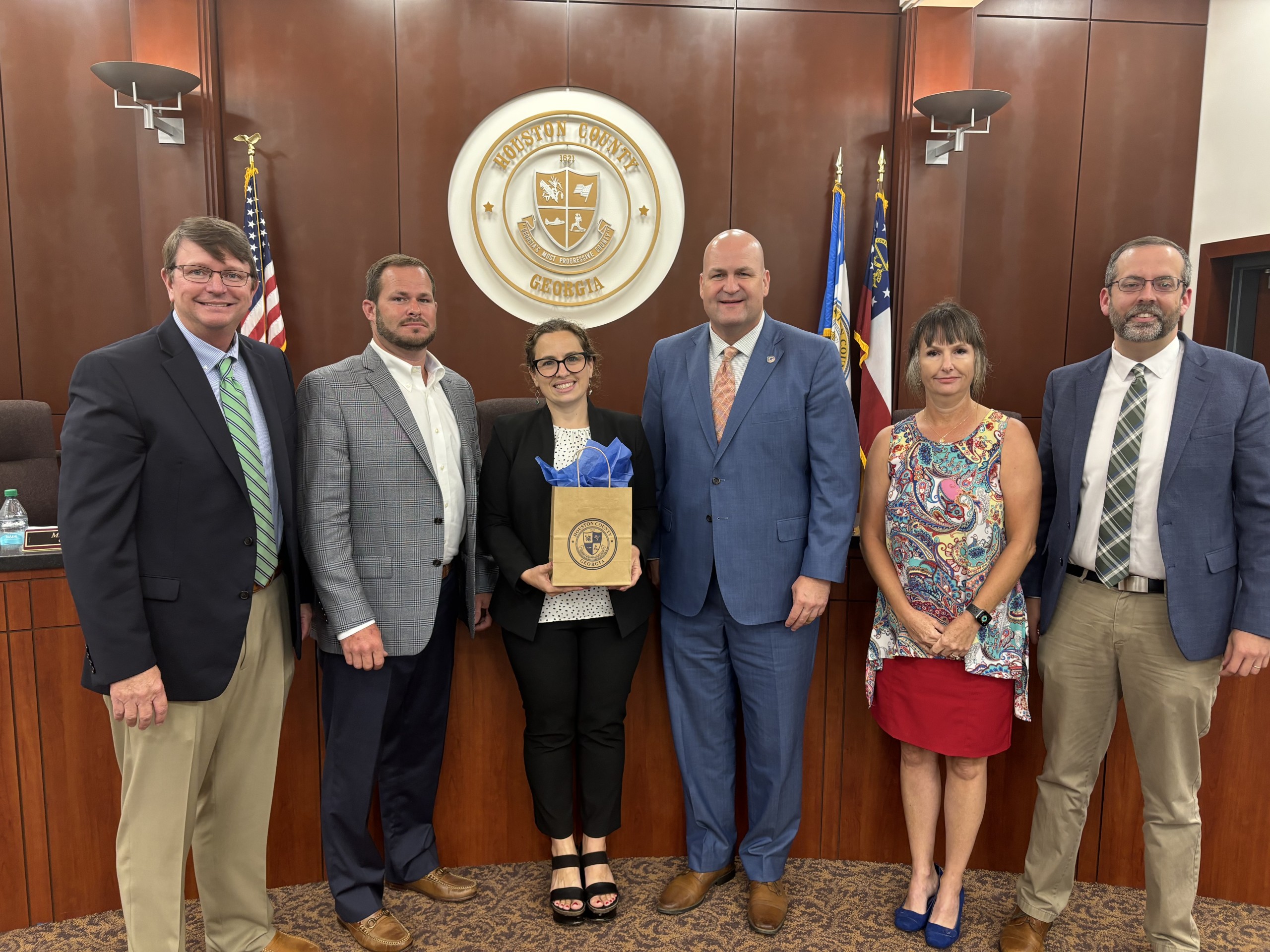 group of four men, two women, woman third from left holding gift bag