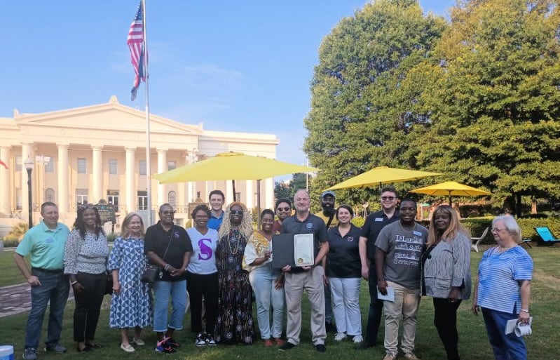 group of people outside in front of trees and a nice building