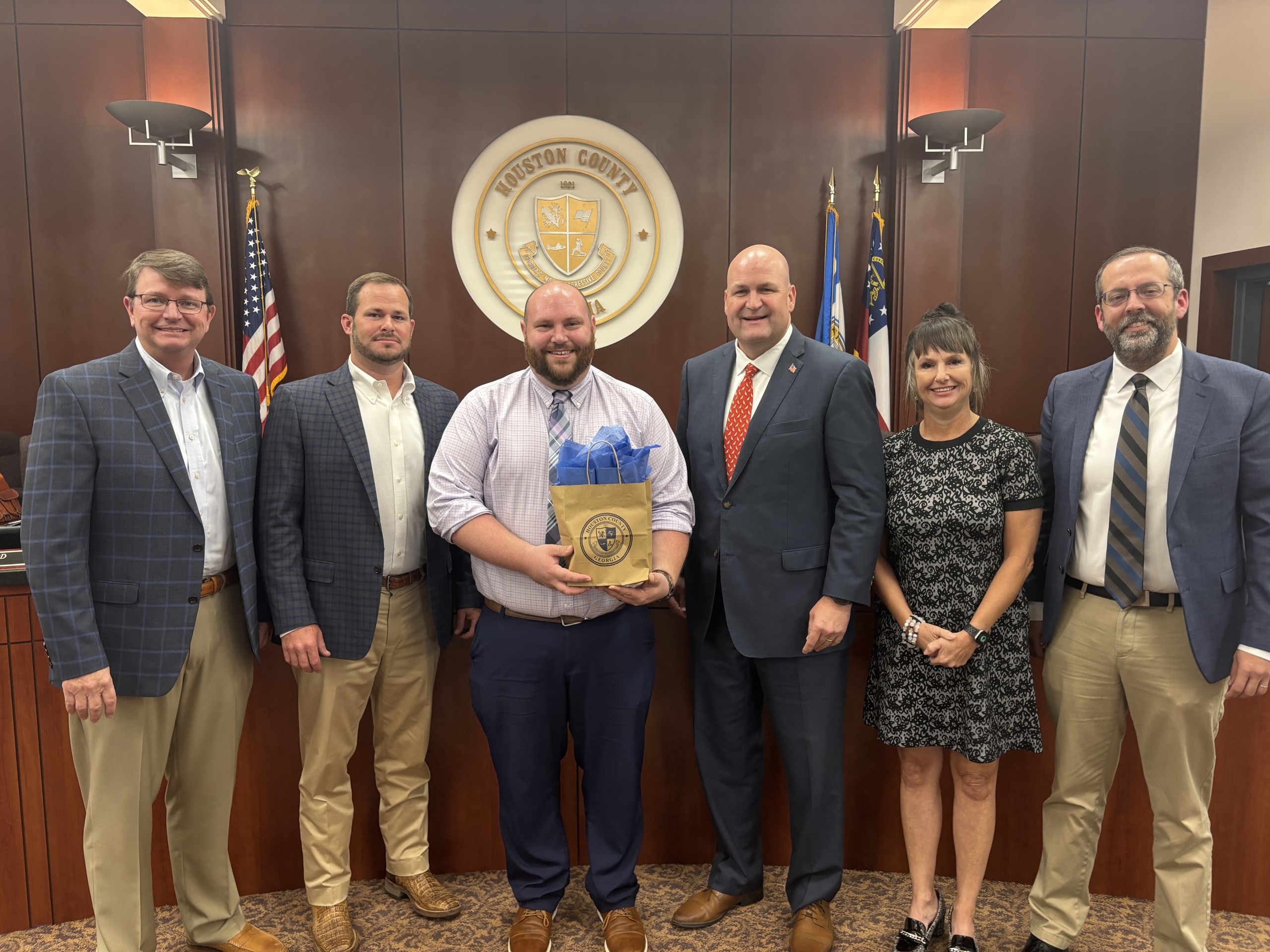 five men, one woman in a group picture; man third from left holding a gift bag