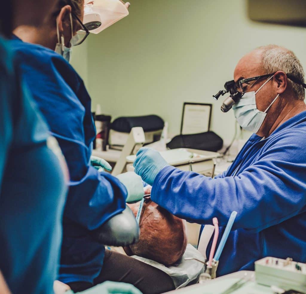 a dentist performs a procedure on a person laying back in a dentist's chair, 