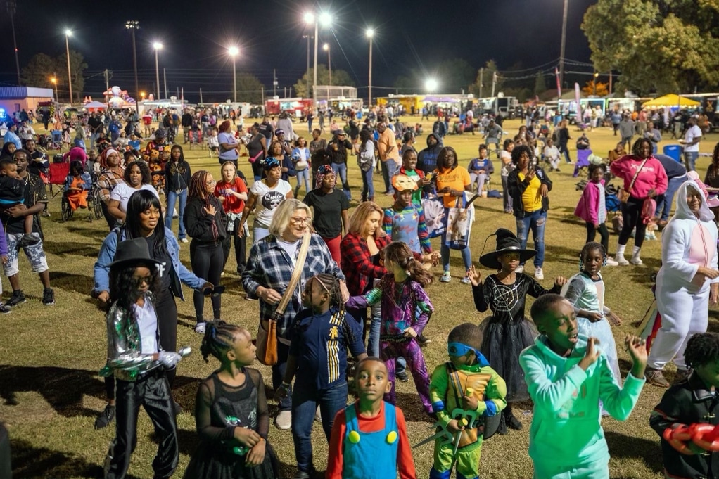 A grassy field at night with a crowd of people, some wearing Halloween costumes.