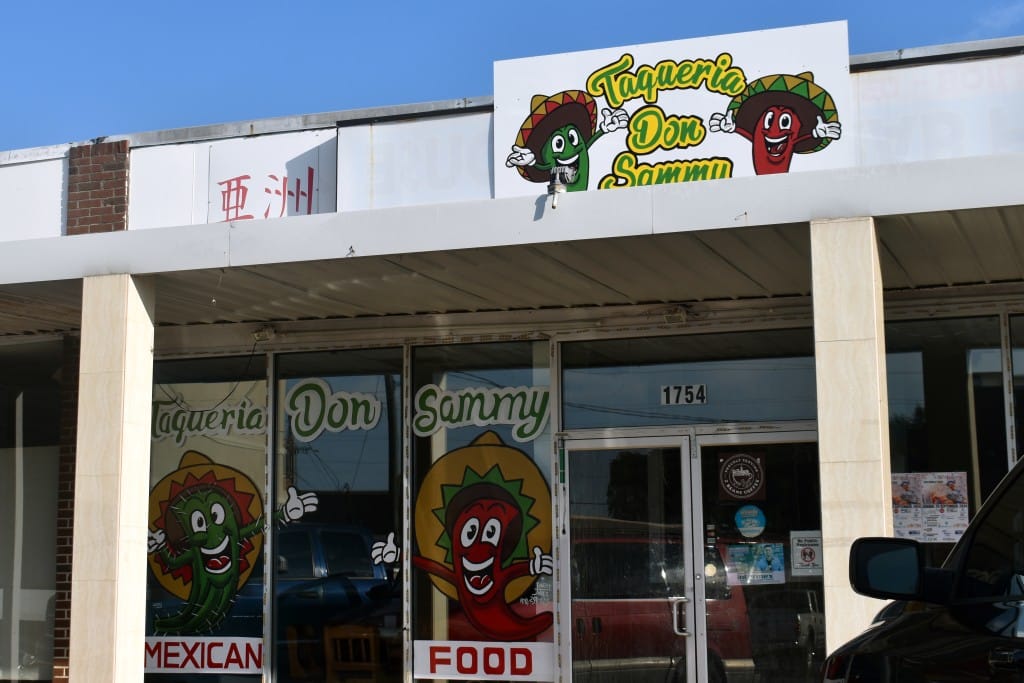 A building with a sign that says "Taqueria Don Sammy" there are red and green pepper caricatures painted next to the sign. 