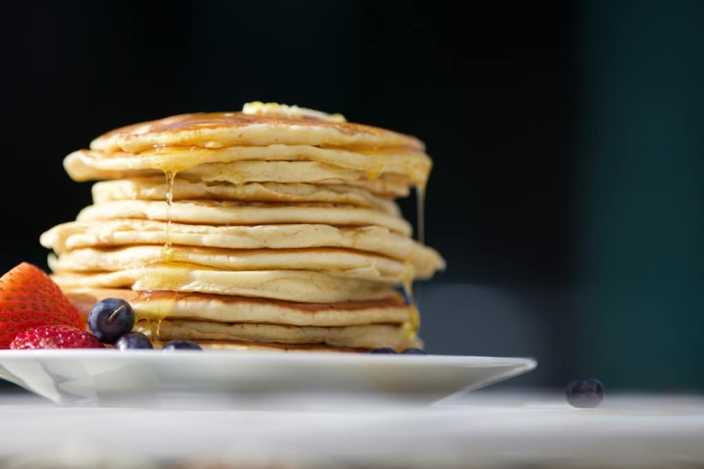 Photo of a stack of pancakes and fruit on the side.