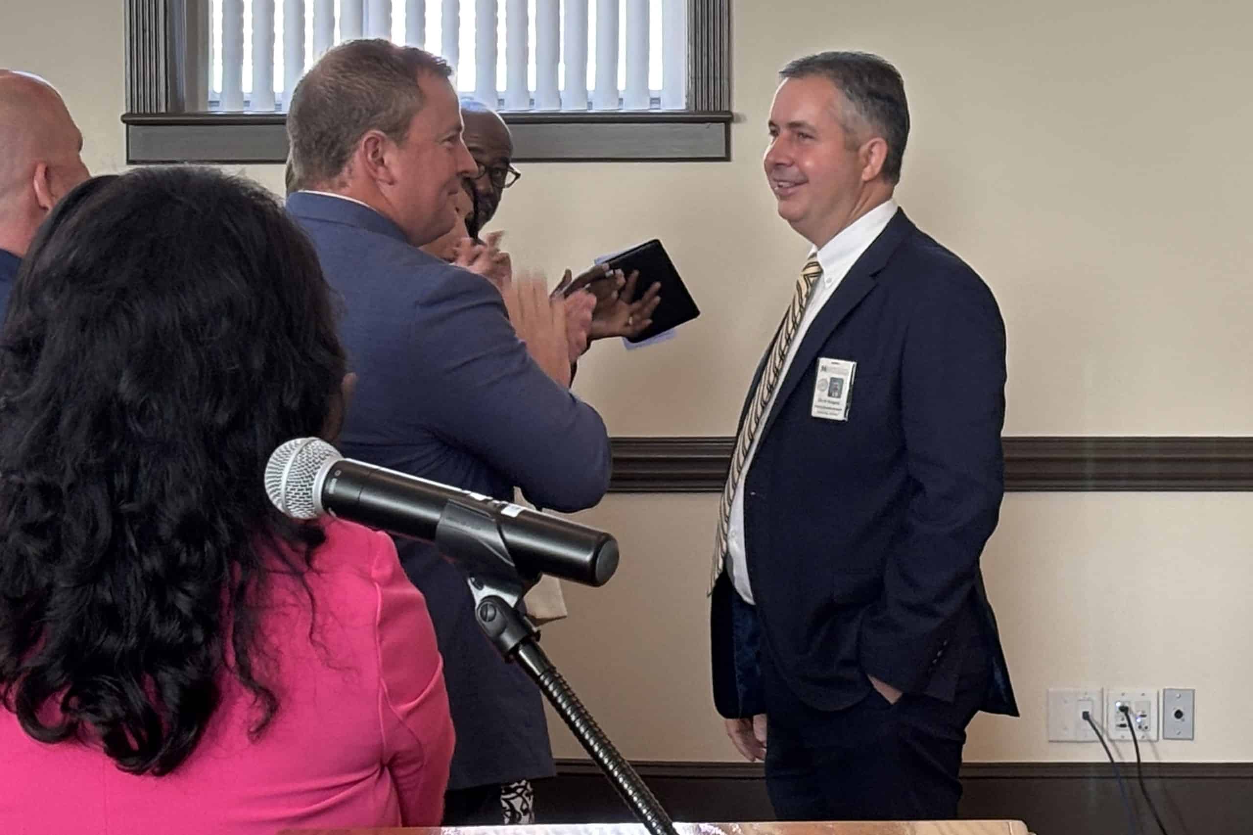 man in suit smiling with a few other clapping for him