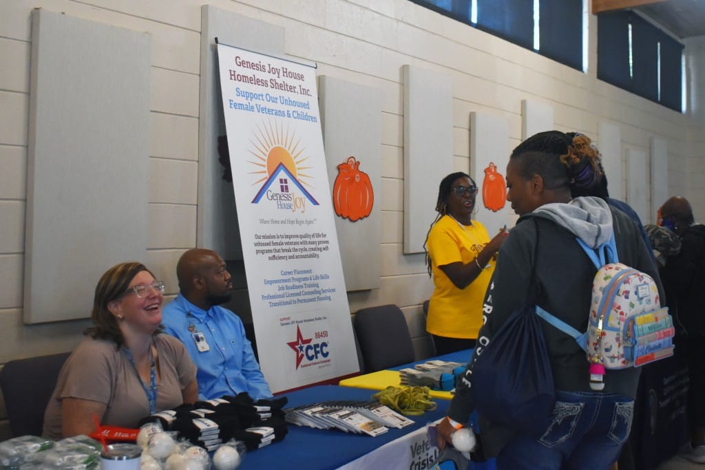 A person is standing in front of a booth. A woman behind the booth is smiling at them.