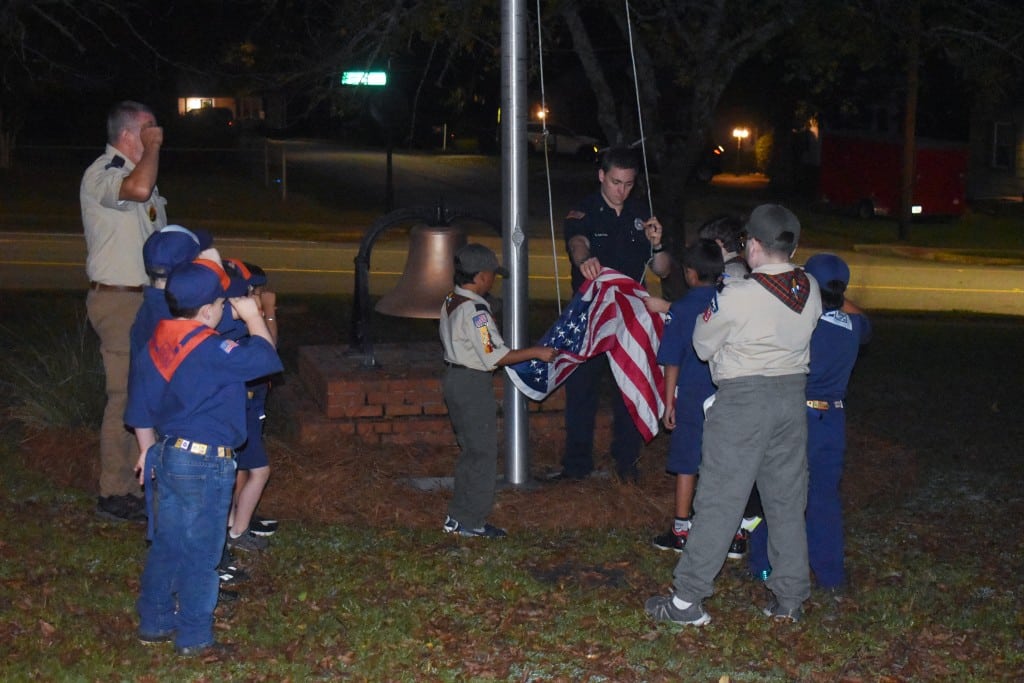 a group of Cub Scouts surrounding a flag pole, folding an american flag.