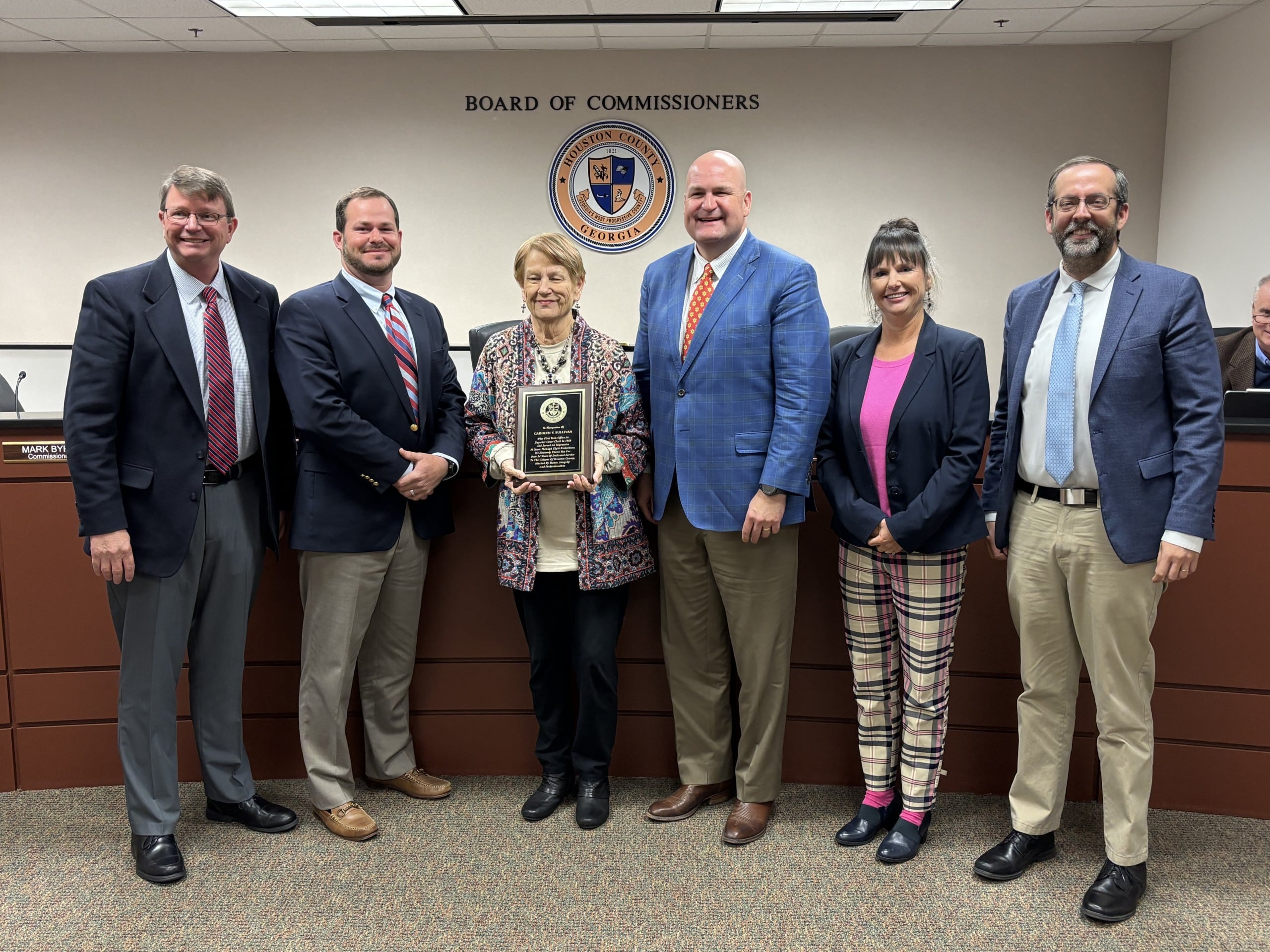 four men wearing suits with two women, women third from left holding a plaque