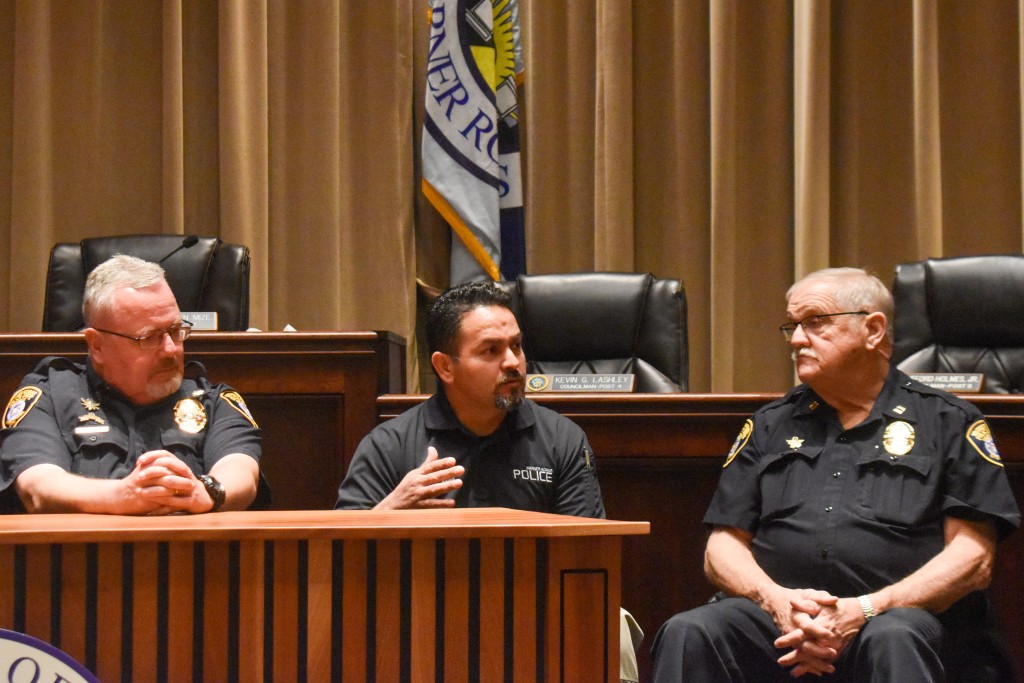Three men sitting at a table. One of the men is addressing a question from the audience.