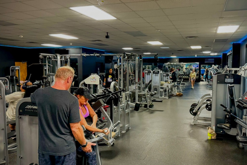A photo of gym equipment. A woman and man are seen working out.