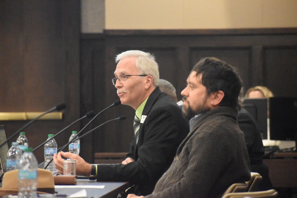 Two men sitting behind a table. One man is speaking into a microphone.
