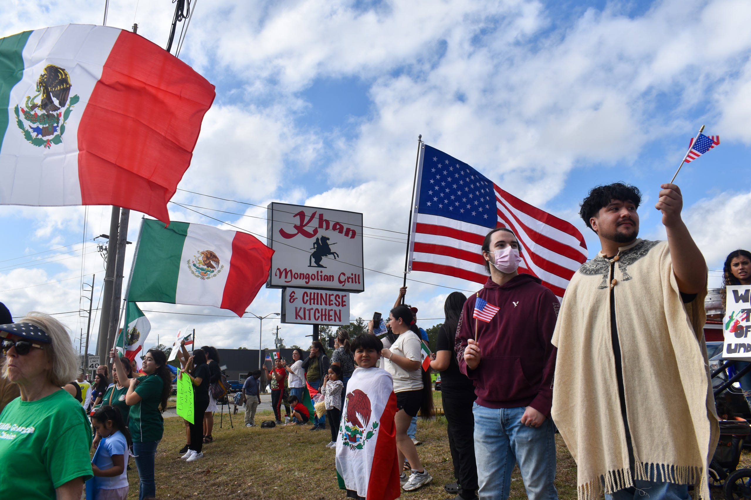 People standing. An American and Mexican flag is seen in the background.
