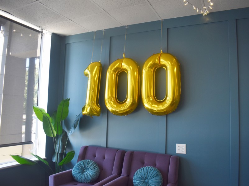 A 100 balloon hanged up above purple seats.