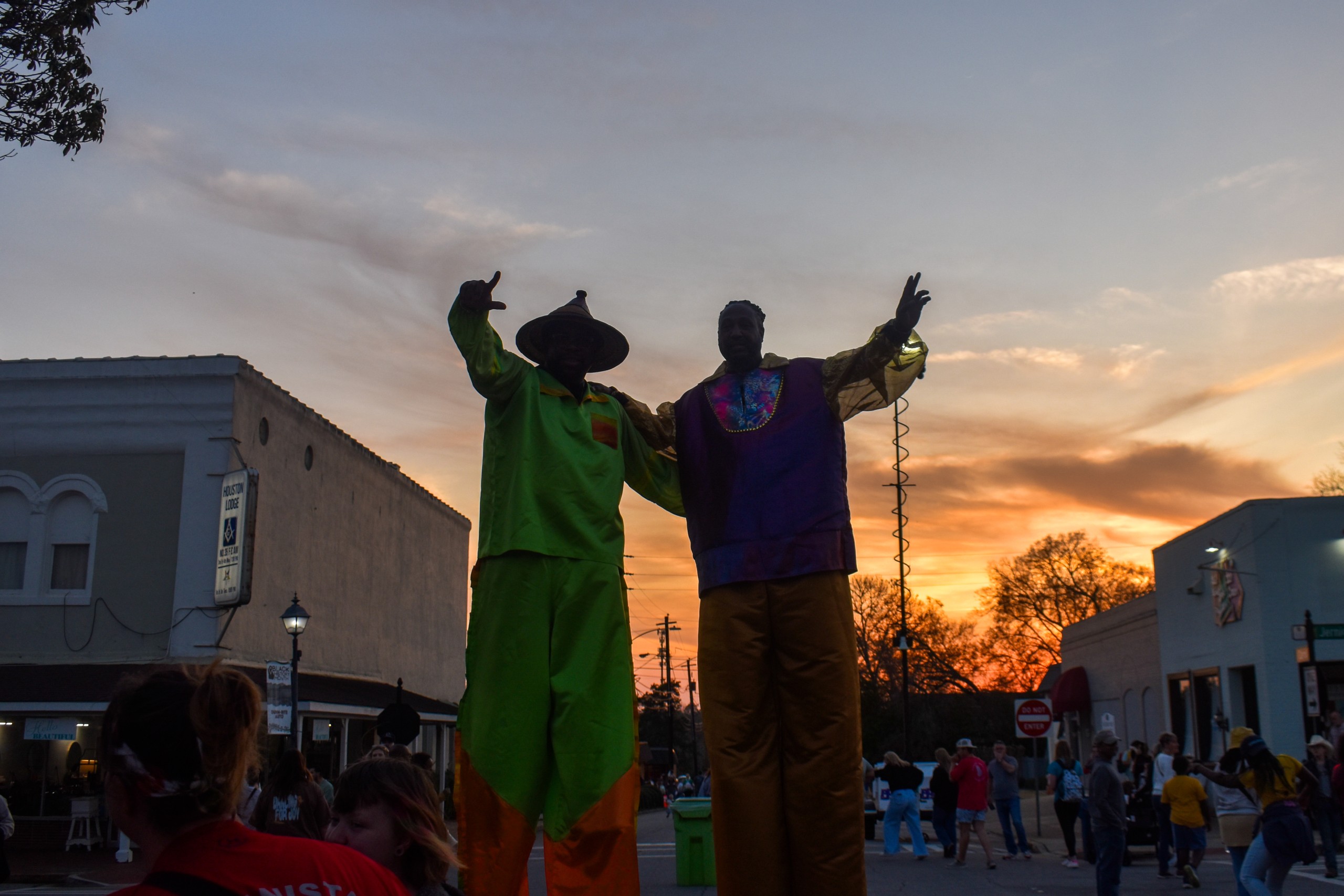 Men in stilts waving. The sunset is seen in the background.