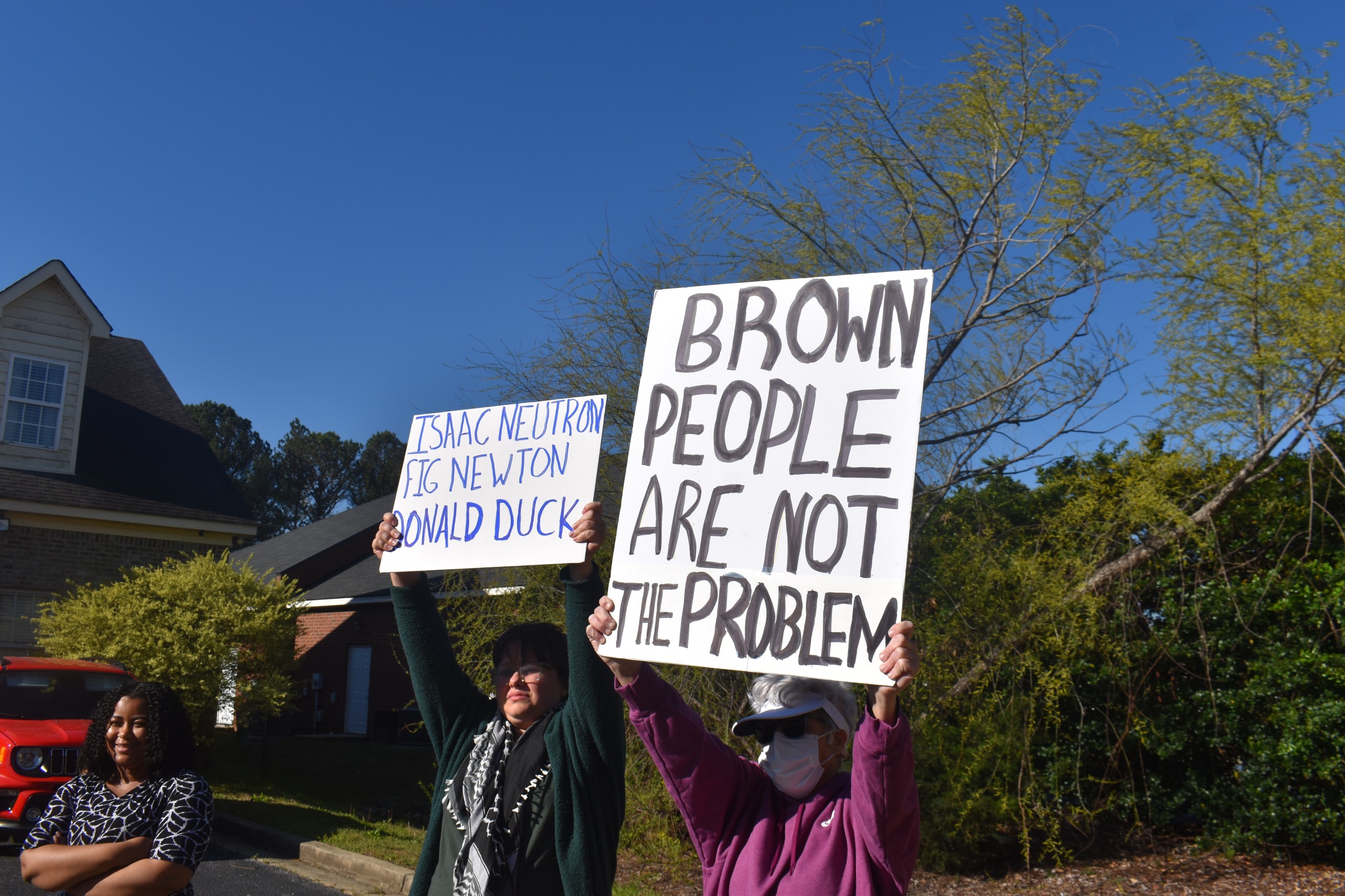 Two women holding up signs. One of the signs says, "Brown people are not the problem."