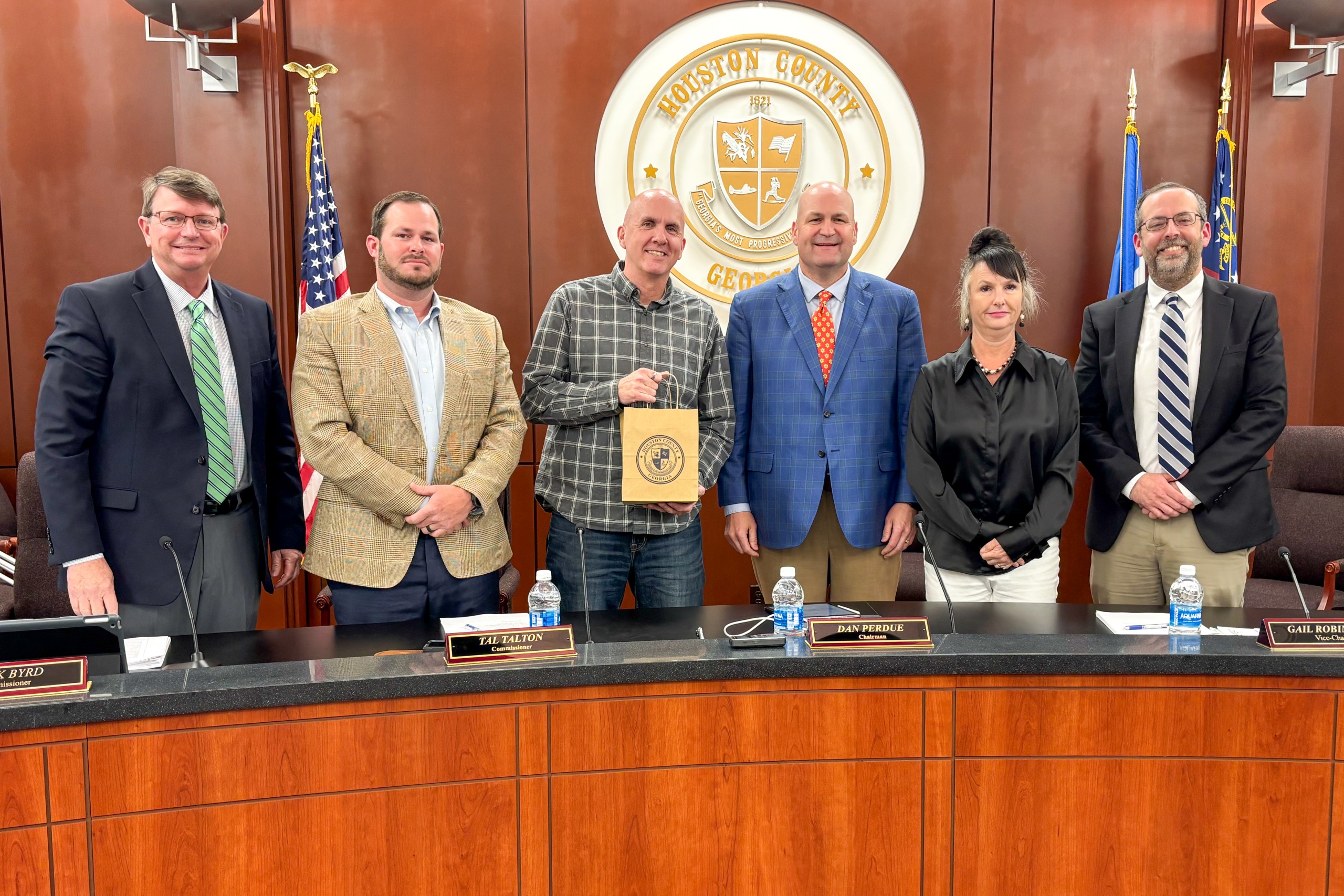 group of five men and one women. man third from left holding a gift bag