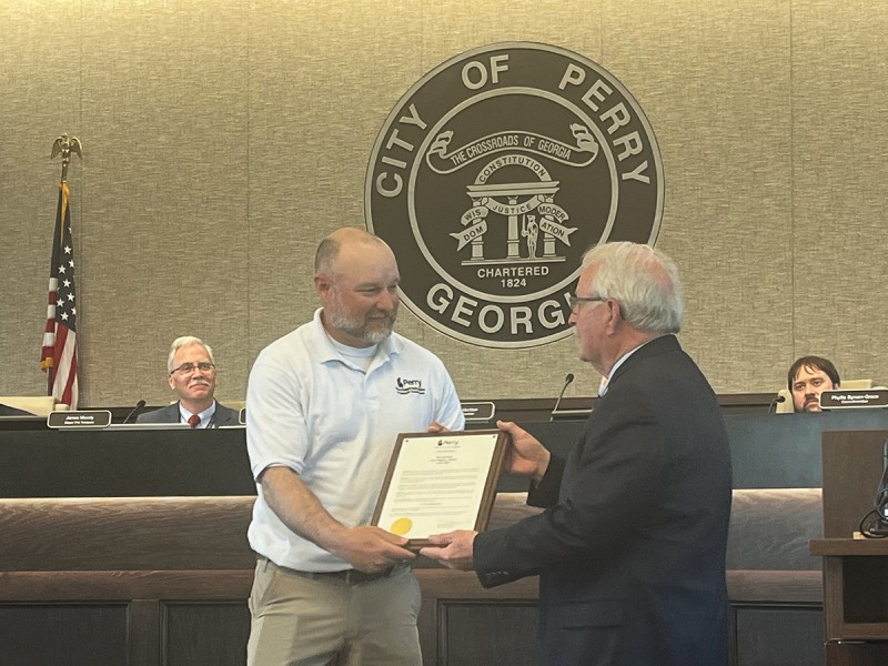 A man in a white shirt receiving a plaque from a man in a a suit.