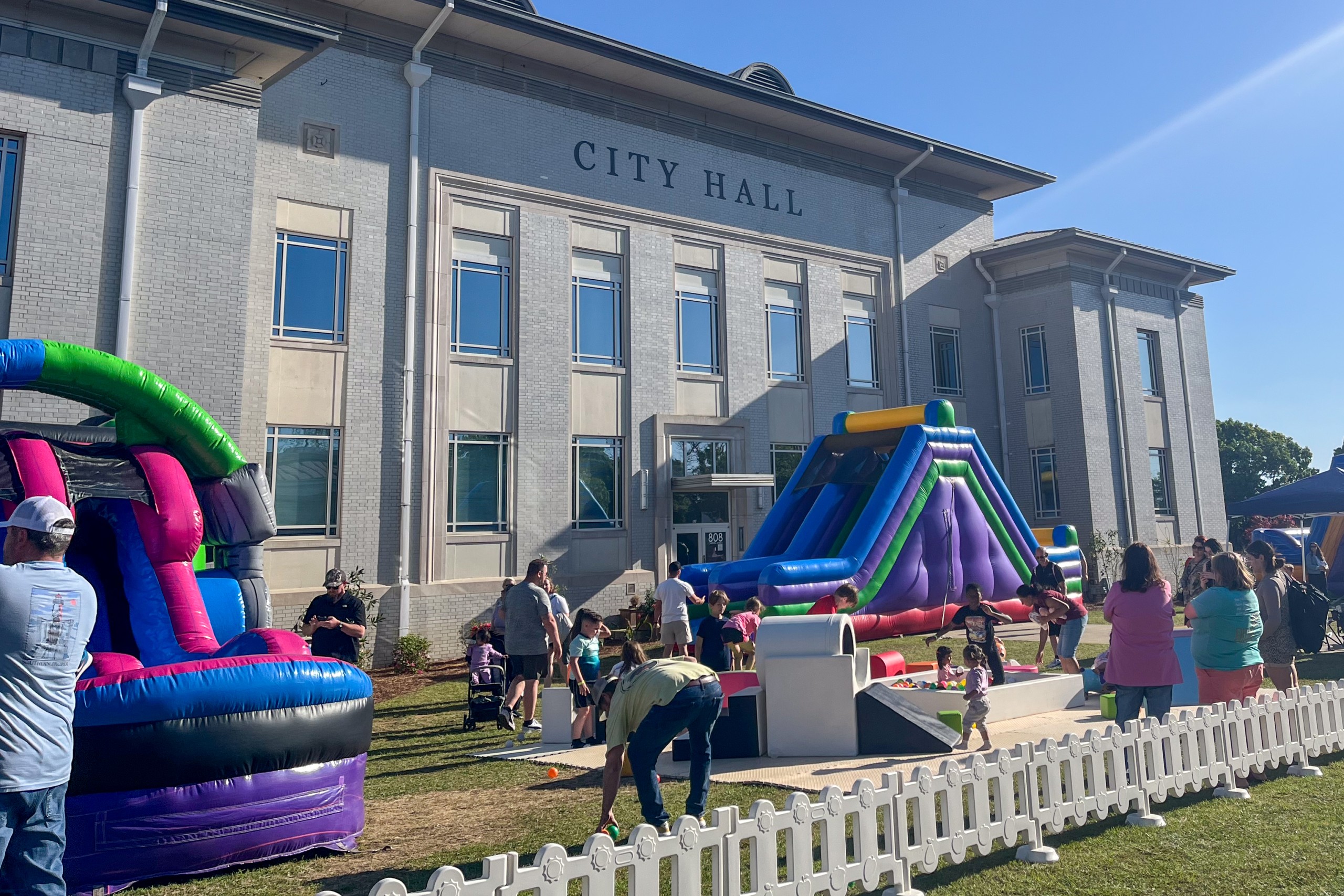Children play on inflatable slides and games outside City Hall during a sunny community event.