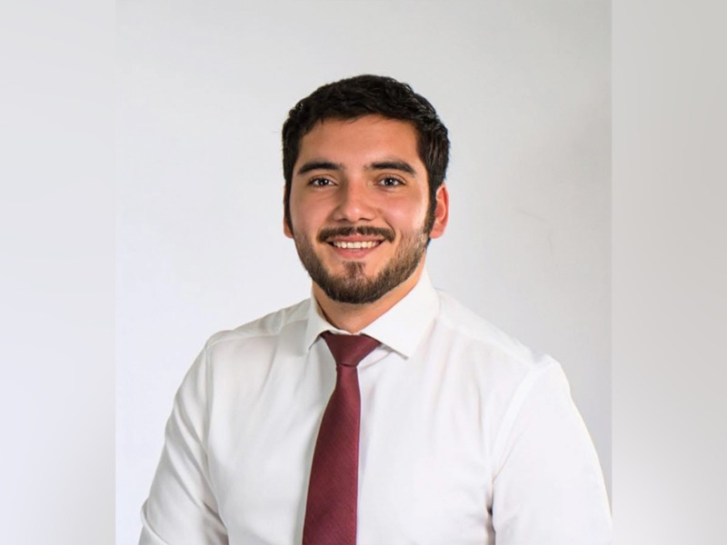 A man in a white button up shirt and red tie smiling.