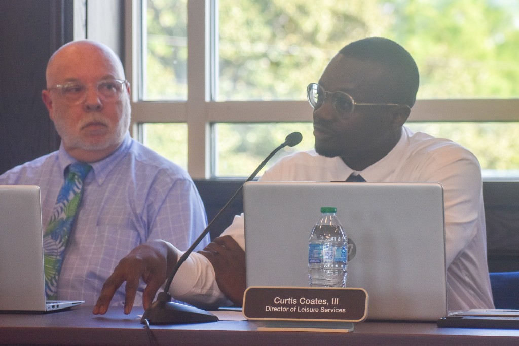 A man sitting down and speaking into a microphone. Another man is seated next to him.