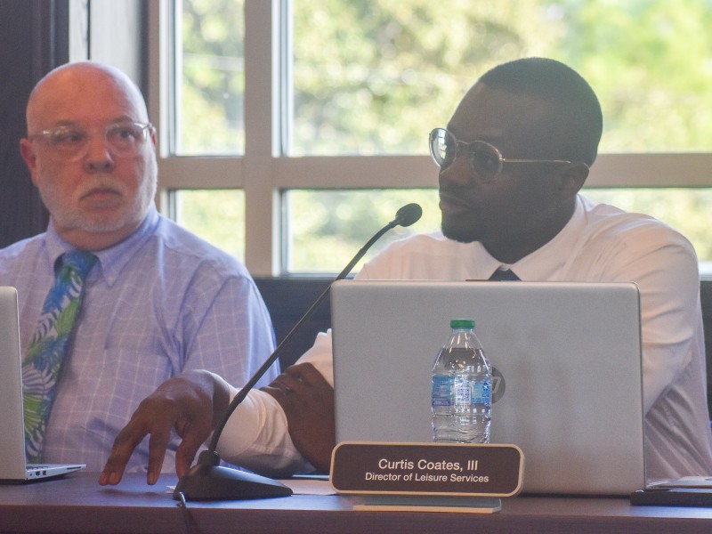 A man sitting down and speaking into a microphone. Another man is seated next to him.