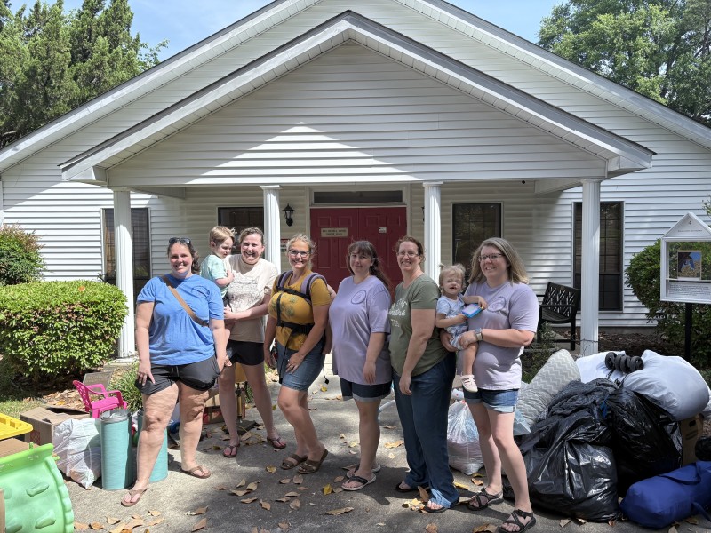 A group of women standing in front of a church. One of the women is holding a baby.