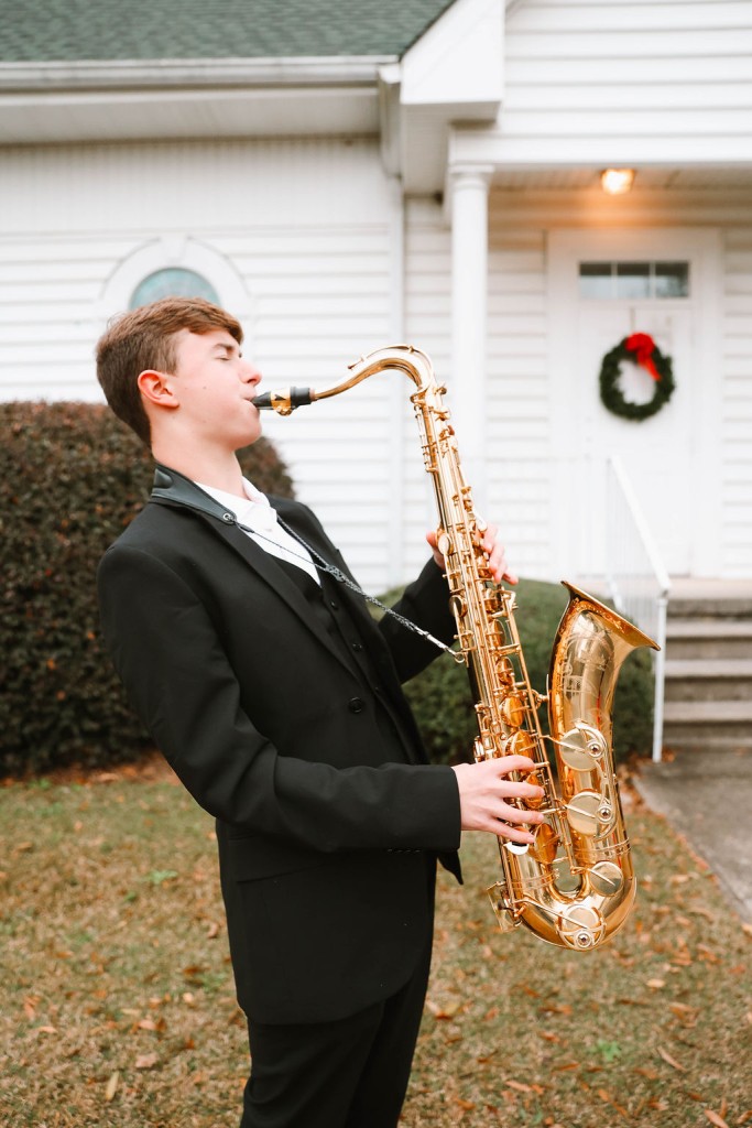 A young man in a tuxedo playing the saxophone.