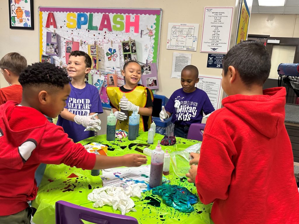 Children gather around a plastic covered table making tie-dye shirts.