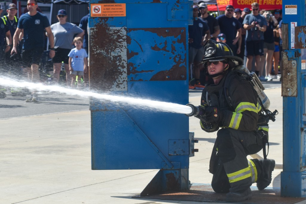 A man dressed in a firefighter uniform spraying a charged hose.