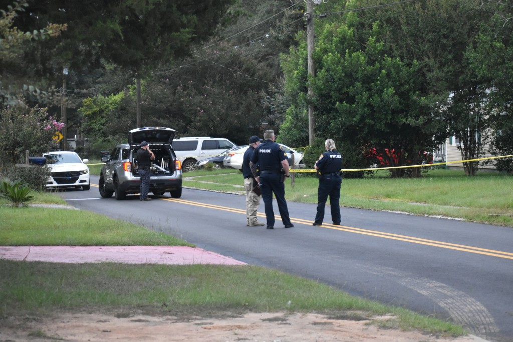 Men in police uniform standing in the middle of a street. A police vehicle is seen in the background.