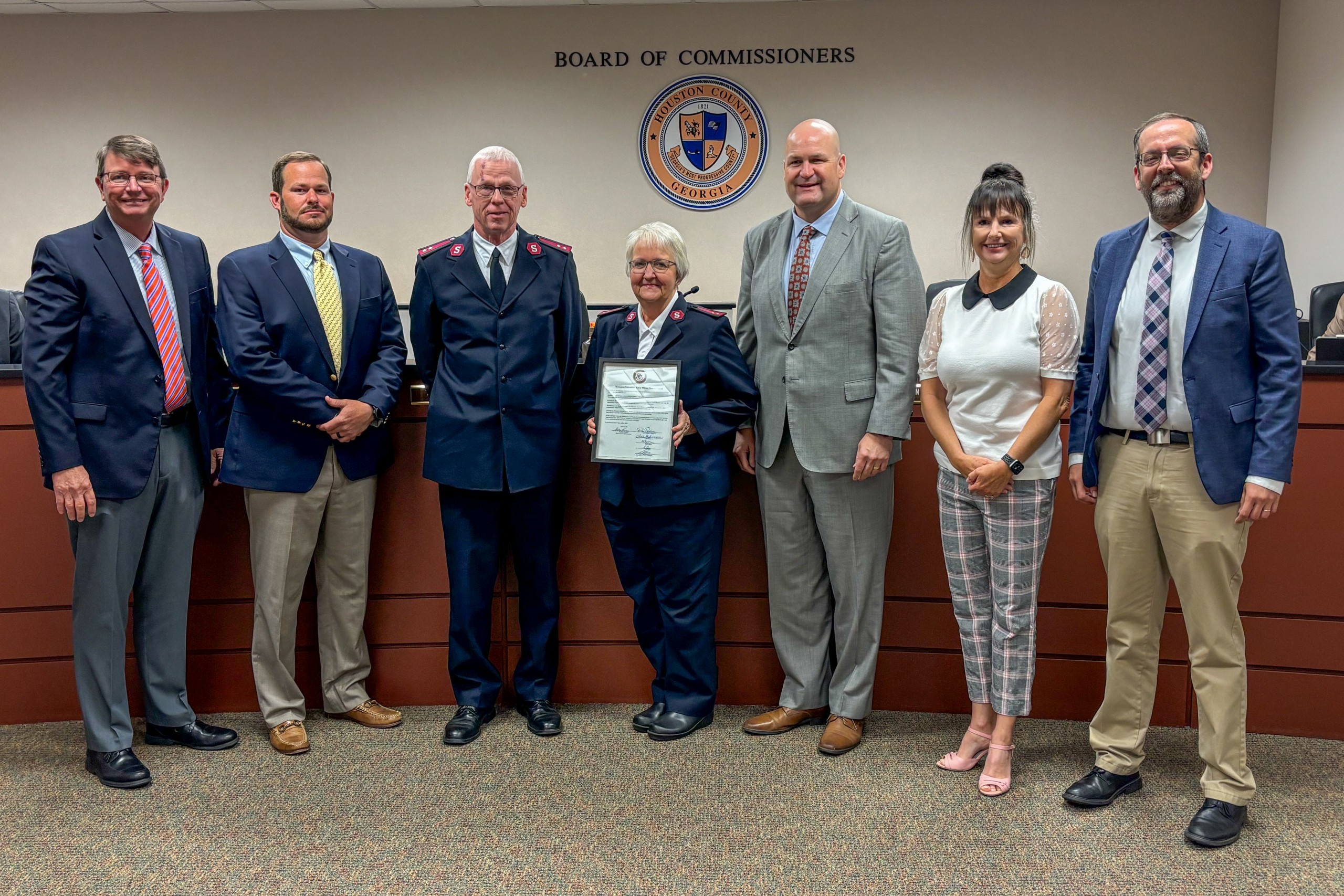 five men, two women, woman in middle holding a proclamation