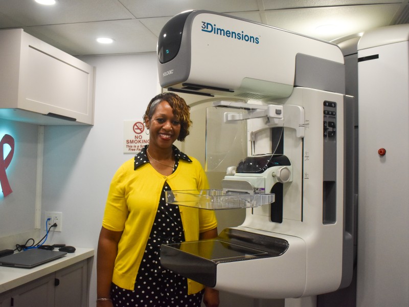A women in a black and white polka dot dress and yellow sweater standing beside a white 3D digital machine.
