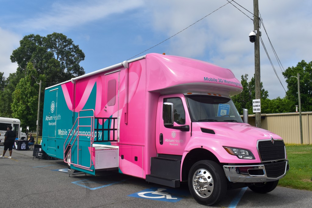 A pink and green bus. People are seen walking in the background.
