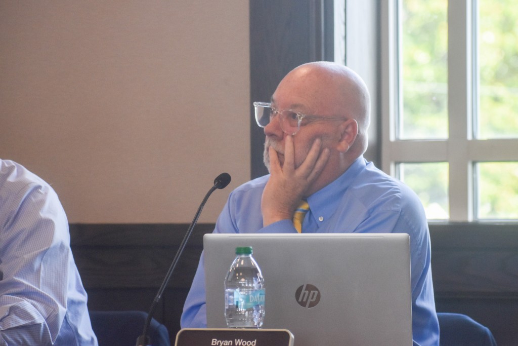 A man with a hand placed on his cheek. He is listening to a discussion.