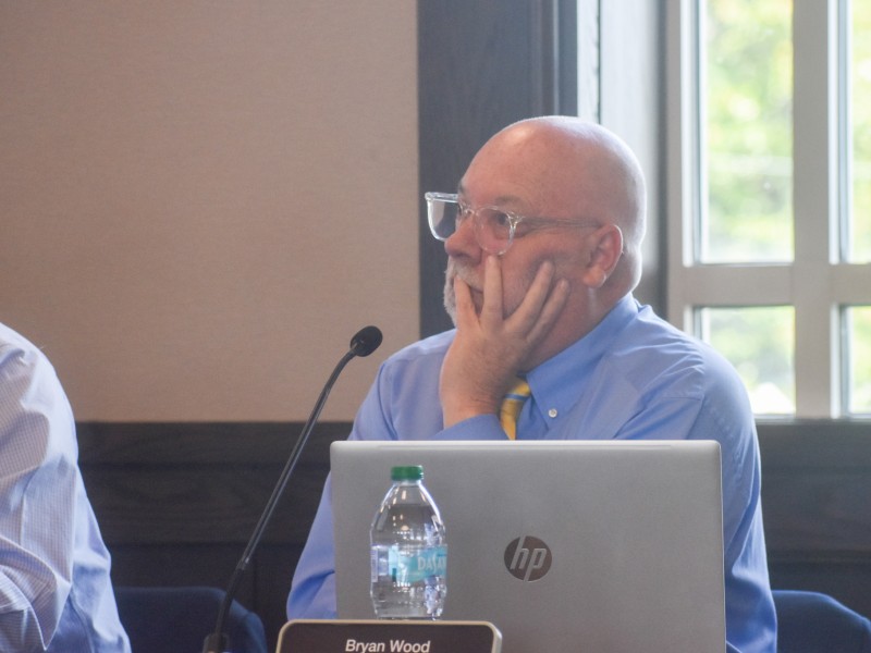 A man with a hand placed on his cheek. He is listening to a discussion.