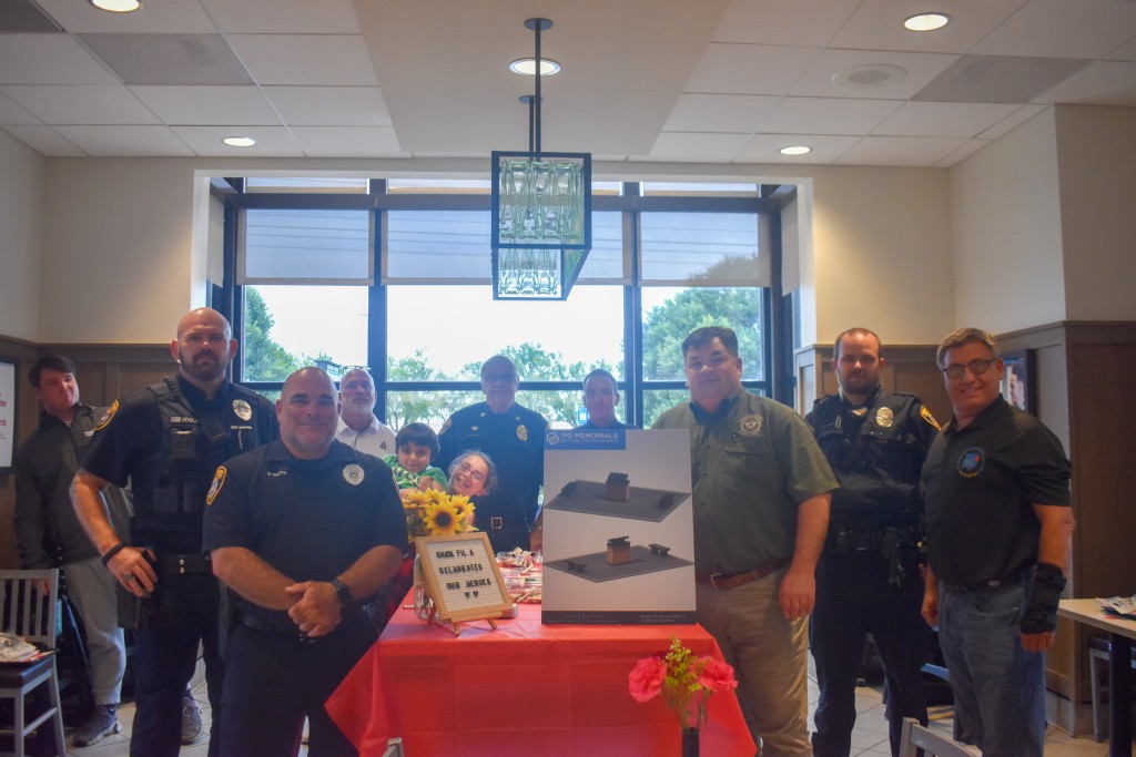 Police officers looking at the camera. There is a red table in the middle and signs on the table.