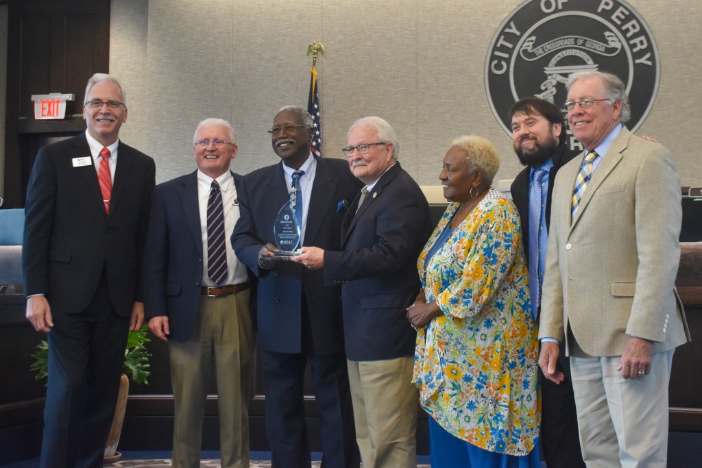 A group of people smiling. Two men in the middle are holding a clear object.