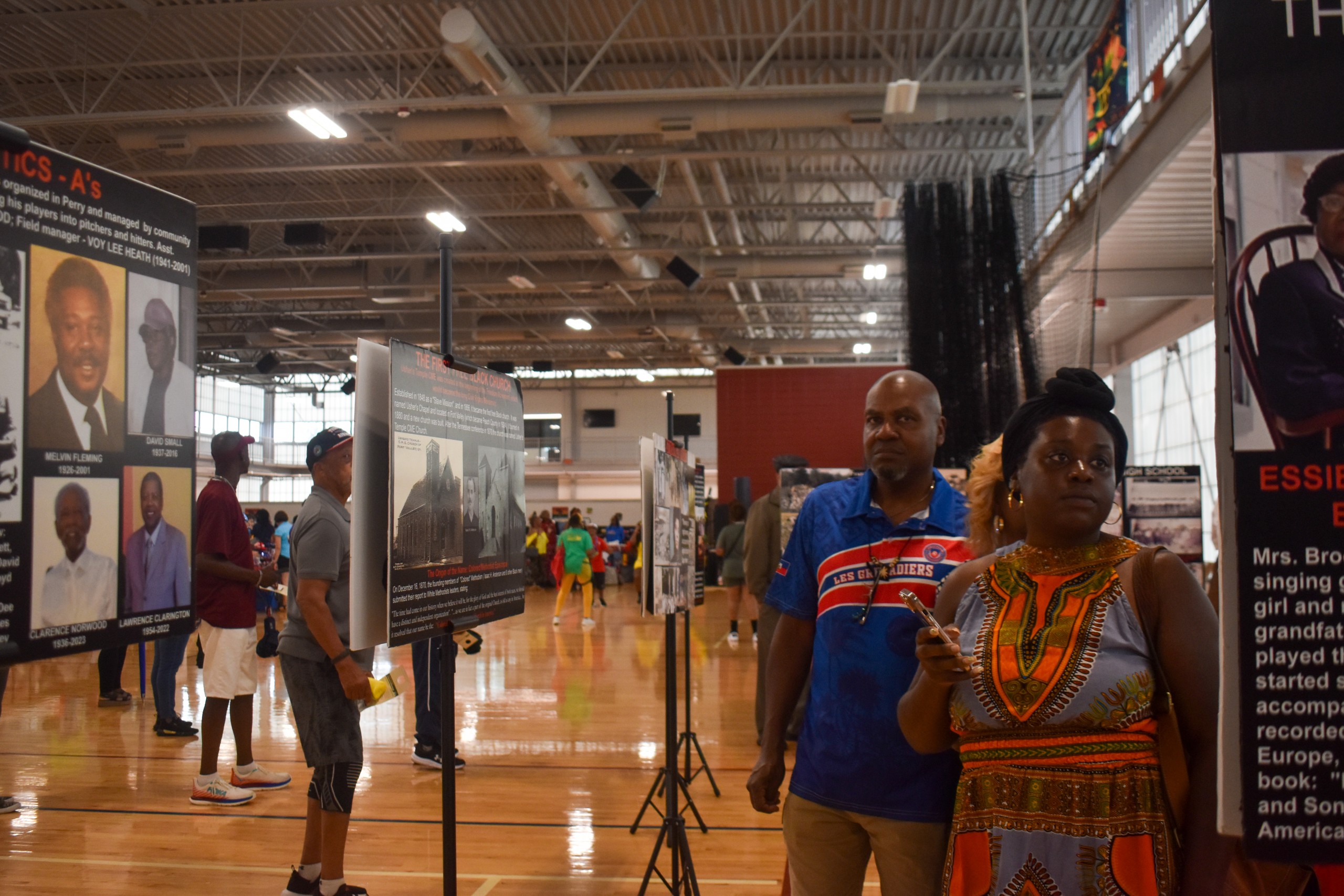A man and a woman facing the camera. Both are looking at a sign and are surrounded by signs.