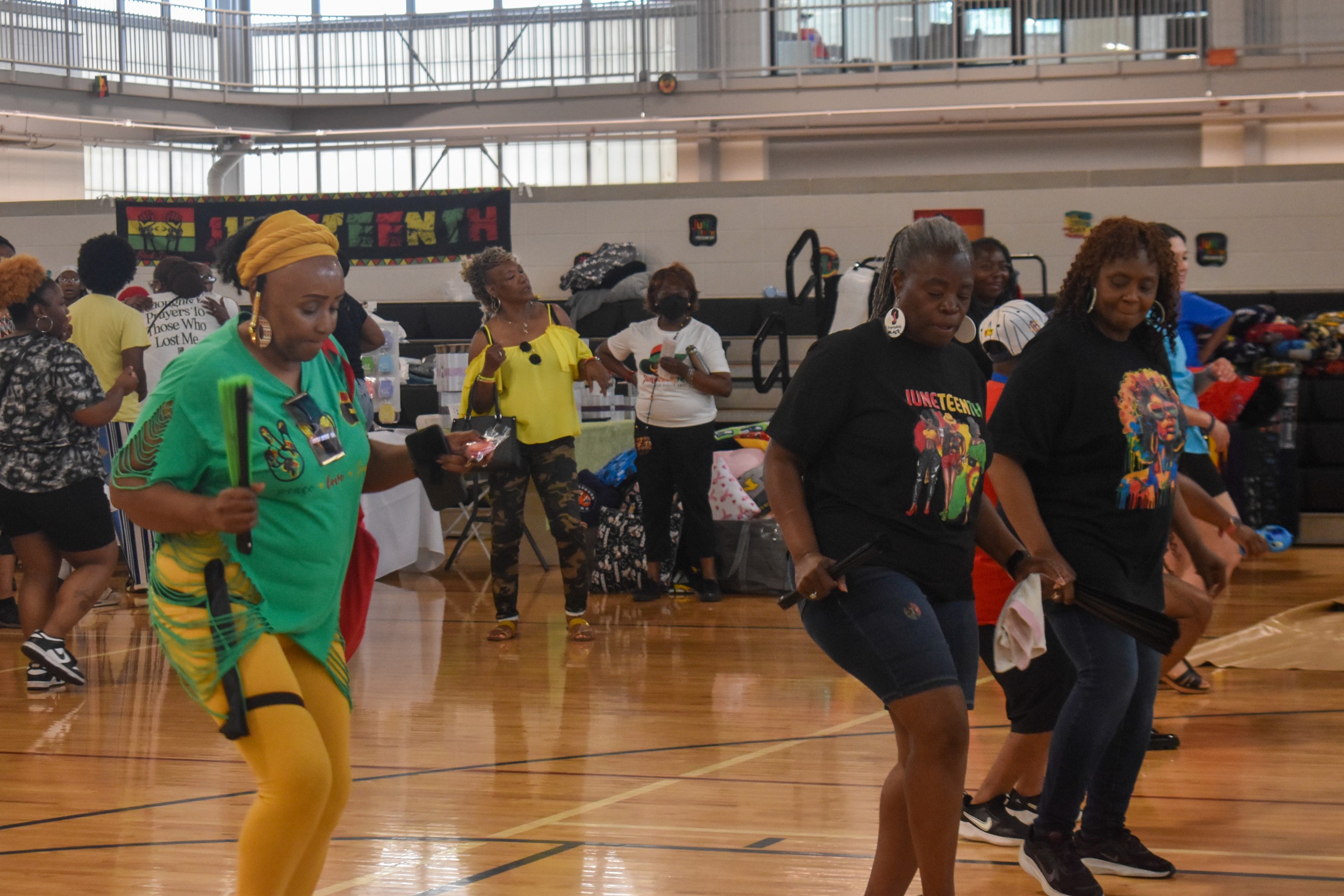 Three women dancing. Two of them are wearing black shirts and one of them is wearing a bright green shirt.