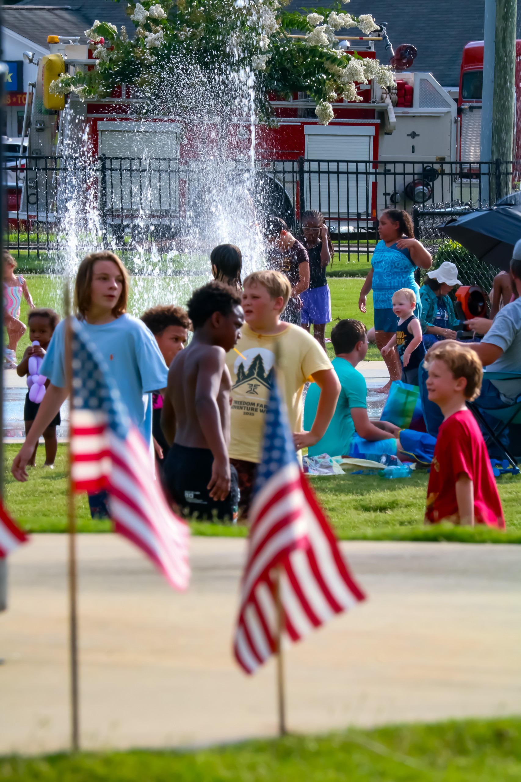 American flags on the grass. In the background, there are children and the slash pad.