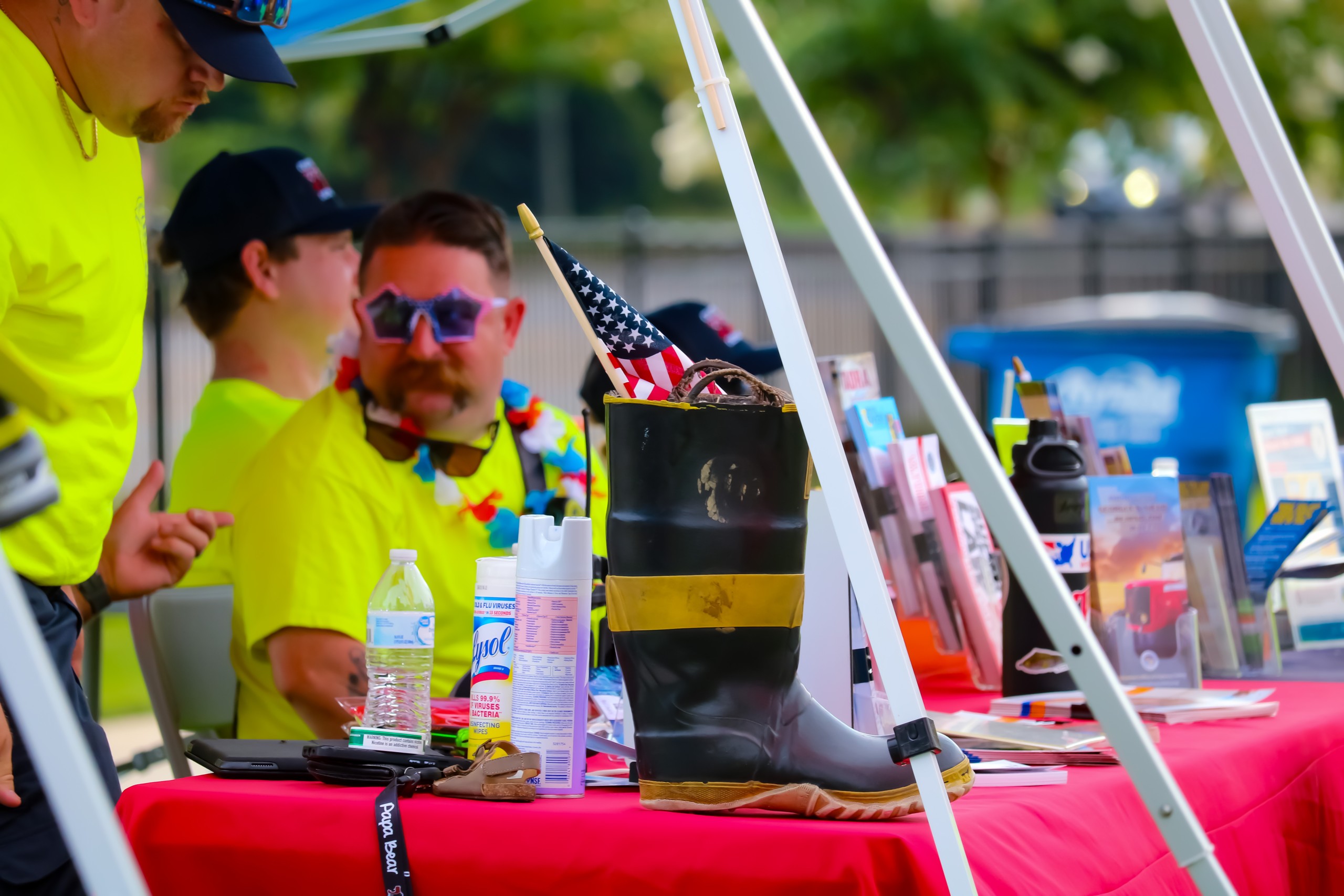 A man in a neon yellow shirt. A firefighter boot is in front of him. In the boot, there is an American flag.