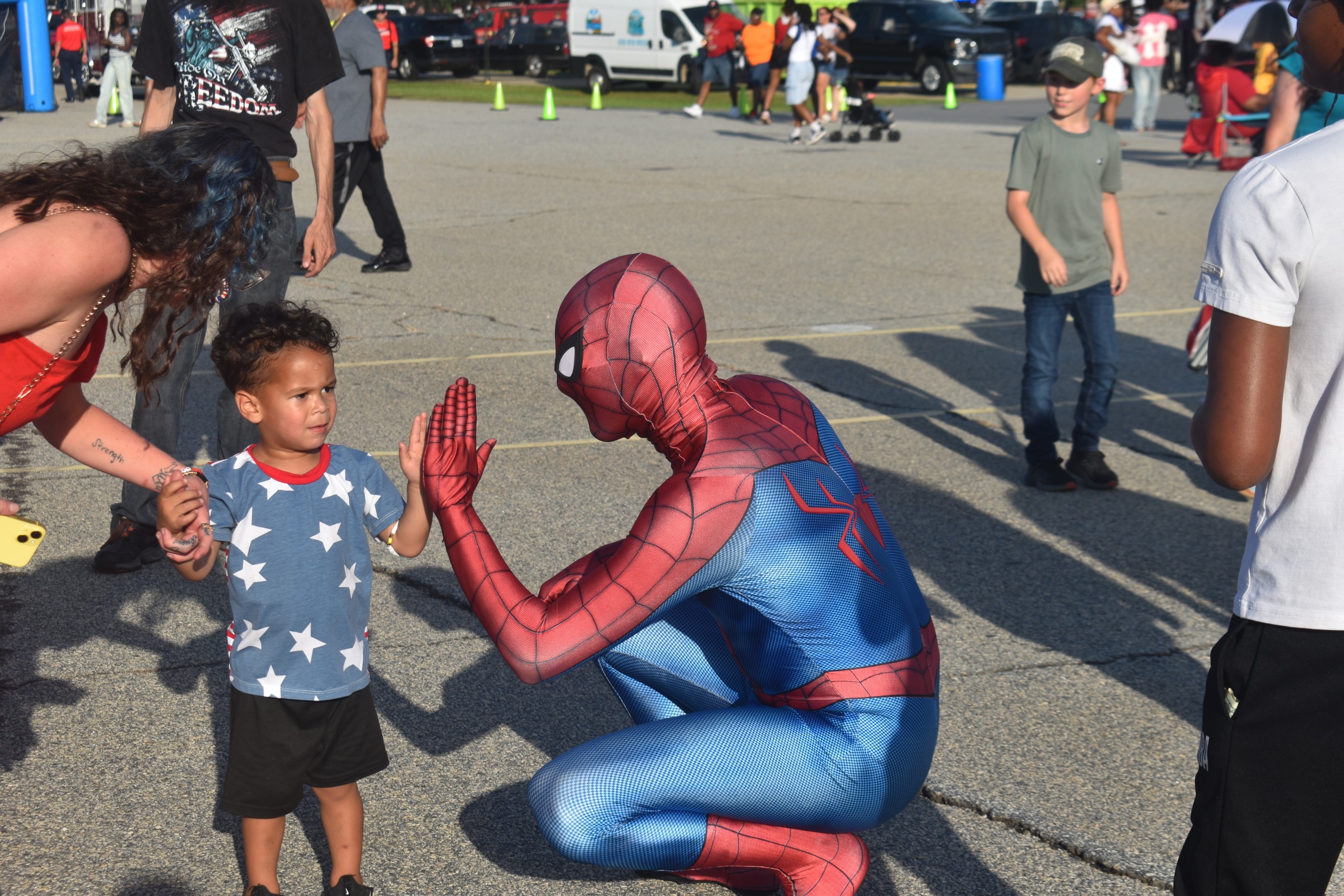 A little boy saying hello to a person dressed as Spider-Man.
