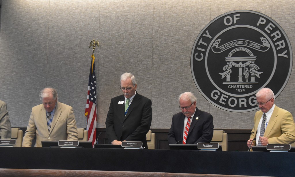 Four men in suits standing with their heads down. They are doing a moment of silence.