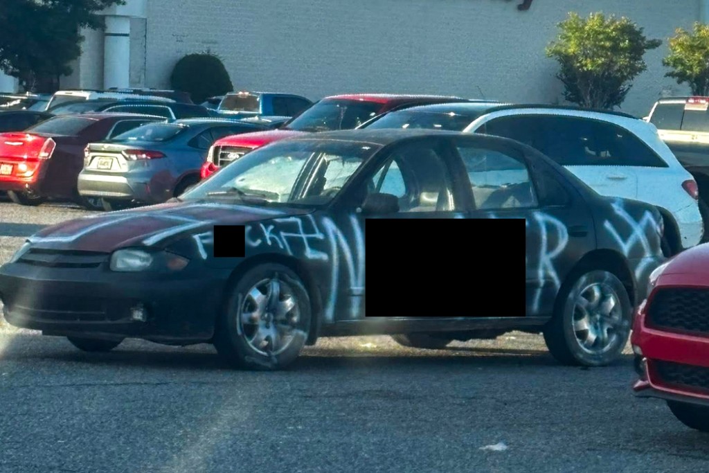 A black car with white letters written on it. The offensive language has been blurred.